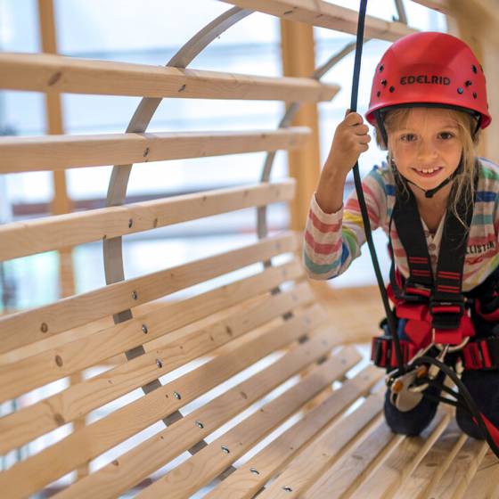 Ein Kind klettert gesichert durch ein Hinderniss im hauseigenen Kletterpark des Familenhotels Feldberger Hof